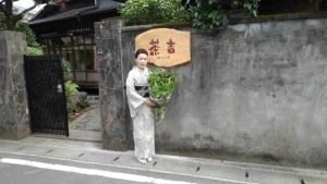 别府Guesthouse Sakichi的站在一堵墙边,拿着一束绿叶的女人