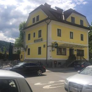 莱奥本Gasthof Knezevic的一座黄色的建筑,前面有汽车停放