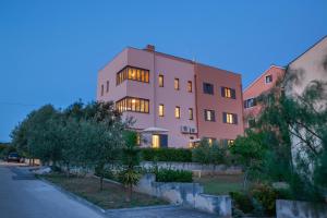 扎达尔Apartments Luana with private jacuzzi的粉红色的建筑,窗户上灯火通明