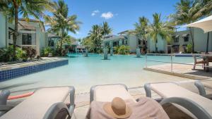 道格拉斯港Luxury Apartments at Temple Resort and Spa Port Douglas的坐在游泳池前椅子上戴帽子的人
