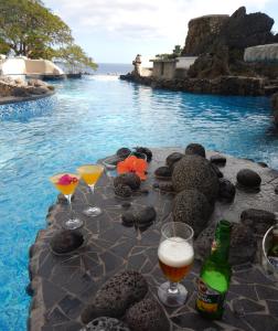 塔纳岛Rockwater Resort的一张桌子,上面放着酒杯,还有一个游泳池