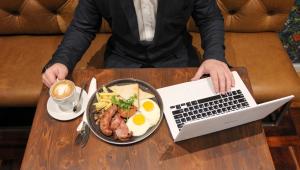 帕罗New National Hotel and Conference的坐在桌子上的人,拿着一盘食物和一台笔记本电脑