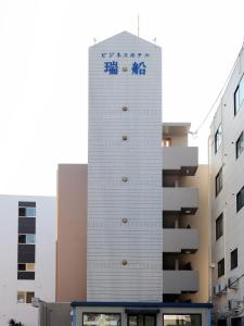 宫崎Tabist Rays Hotel Suisen的一座高大的白色建筑,上面有标志