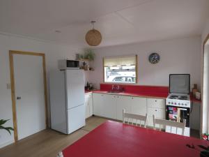 旺阿雷Pohutukawa Bach的厨房配有白色冰箱和红色台面