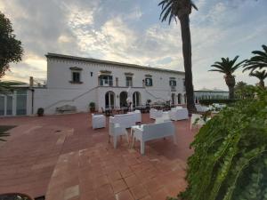 锡拉库扎Resort Villa Isola B&B的一座配有白色桌椅和棕榈树的建筑