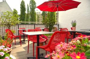 慕尼黑Lizz Hotel Munich的庭院配有红色椅子和一张带遮阳伞的桌子。