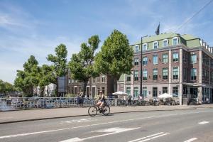 阿姆斯特丹诺丁山精品酒店的一名妇女骑着自行车沿着建筑物旁边的街道骑着
