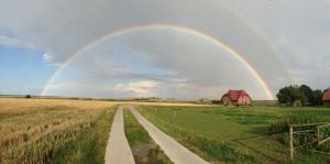 旺格兰Ferienhof Schild FeWo Bullerbü的一条有路和谷仓的田野上的一个彩虹