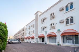 马斯喀特Hotel Summersands Al Wadi Al kabir的一座白色的大建筑,前面有汽车停放