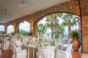 勒托阳尼Hotel Olimpo le Terrazze的宴会厅配有白色的桌椅和棕榈树