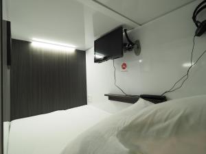 船桥市Leo Yu Capsule Hotel Funabashi的卧室配有白色的床和墙上的电视。