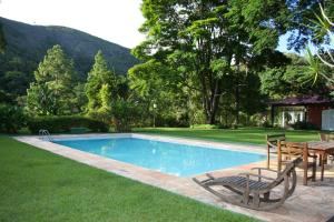 伊泰帕瓦Pousada Quinta dos Pássaros Itaipava的庭院旁的游泳池配有桌椅