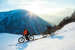 塞斯特雷Hotel Club Uappala Sestriere的两个人骑着自行车沿着雪覆盖的山下骑行
