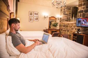 库斯科阿拉纳库斯科精品酒店的坐在床上的男人使用笔记本电脑