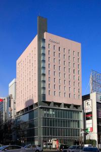 仙台里士满酒店普利米尔仙台站前的一座高大的建筑,前面有汽车停放