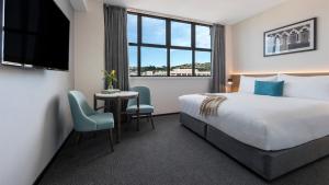 惠灵顿Oaks Wellington Hotel的酒店客房带一张床、一张桌子和椅子