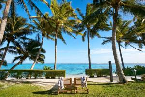 拉罗汤加Motu Beachfront Art Villas的棕榈树海滩上的桌椅