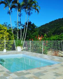 塞拉内格拉Pousada Primavera da Serra的棕榈树围栏前的游泳池
