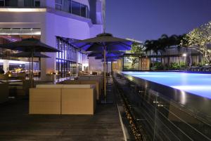 曼谷JC Kevin Sathorn Bangkok Hotel的一座带桌子和遮阳伞的游泳池位于一座建筑旁边