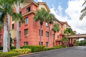 棕榈滩花园温莎花园贝斯特韦斯特PLUS套房/会议中心酒店的前面有棕榈树的粉红色建筑