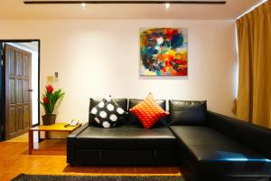 曼谷沙吞塞丽娜套房公寓的客厅里一张黑色皮沙发,配有绘画作品