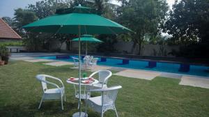 纳西克Jungle Safari Resort & Holiday Villa的一张桌子和椅子,旁边是一座游泳池,上面有一把绿色遮阳伞