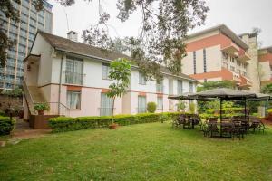 内罗毕ACK Guest House Nairobi的建筑前的院子,配有桌子和遮阳伞