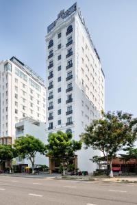 岘港Roliva Hotel & Apartment Danang的一条高大的白色建筑,在街道前有树木