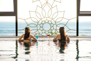岘港Eden Ocean View Hotel Da Nang的两个女人在无边泳池里,有彩色玻璃窗