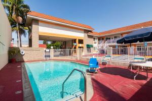 阿蒂西亚Rodeway Inn Artesia Cerritos的酒店前的游泳池配有桌子和遮阳伞