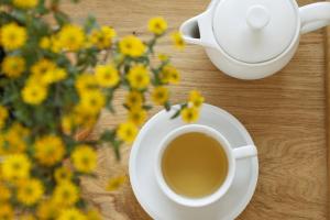 曼德沙伊德Landhotel Pension Haus Sonneck的一杯咖啡在桌子上,种上黄色的花