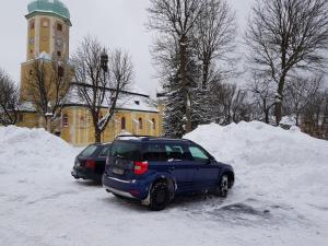 上布拉特纳Apartman Náměstí的两辆停在大楼前雪地里的汽车