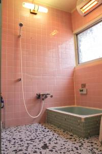 玉野市虎所里特旅馆的粉红色的瓷砖浴室设有浴缸和窗户。