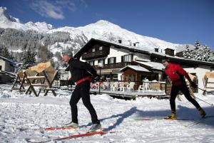 达沃斯达沃斯班达酒店的两个男人在雪中滑雪,在小屋前