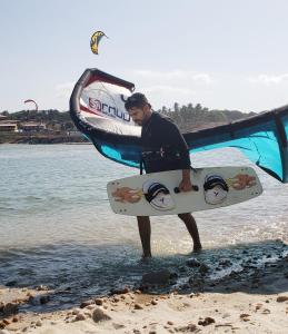 卡姆布库Pousada Brasil Cumbuco的站在海滩上,拿着冲浪板的人