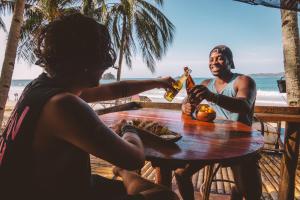 爱妮岛Mad Monkey Hostel Nacpan Beach的两人坐在海滩上桌边喝啤酒