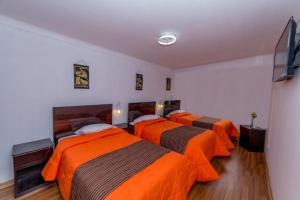 库斯科Hotel Peru Real的配有橙色床单的客房内的三张床
