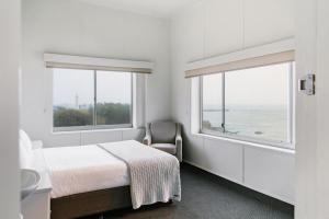 扬巴Pacific Hotel Yamba的一间卧室配有一张床和一把椅子,还有两个窗户