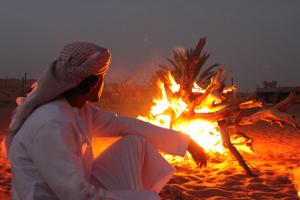 Al WāşilNomadic Desert Camp的坐在海滩 ⁇ 火旁的女人