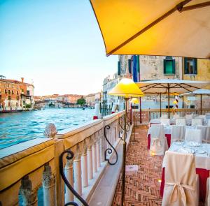 威尼斯帕拉佐斯特恩酒店的一间位于水边的餐厅,配有桌子和遮阳伞