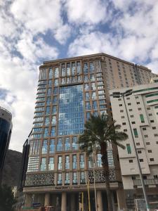 麦加Violet Al Azizia Hotel的一座高大的建筑,前面有一棵棕榈树