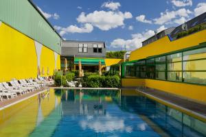 维也纳Vienna Sporthotel的一座黄色建筑旁的游泳池,配有椅子