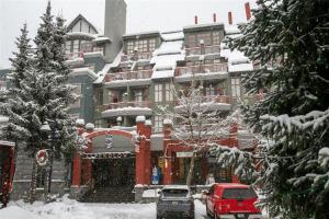 惠斯勒比尔阿尔派格洛夫公寓式酒店的一座被雪覆盖的建筑,前面有汽车停放