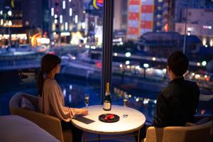 福冈The OneFive Villa Fukuoka的坐在桌子旁的男人和女人,喝一瓶葡萄酒