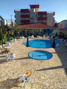 瓜拉图巴Hotel Rota do Sol的大楼前的游泳池配有遮阳伞和椅子