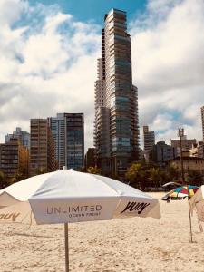 桑托斯Unlimited - Frente ao Mar. Apt todo mobiliado.的海滩上高高的建筑上的白色遮阳伞