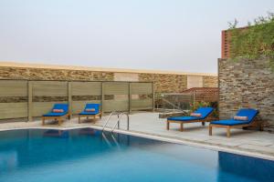 吉达吉达网关假日酒店的一座带蓝色椅子的游泳池,位于大楼旁