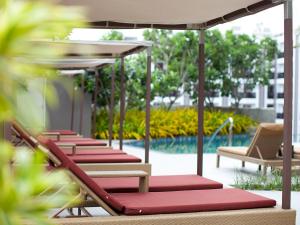 芭堤雅市中心芭堤雅美居海洋度假酒店的一排躺椅、一把遮阳伞和一个游泳池