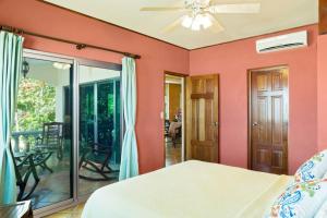 里瓦斯Villas Iguana A-2 Beachfront Condo的一间卧室设有粉红色的墙壁和一张带吊扇的床。