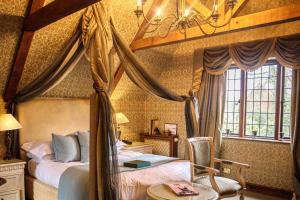 霍利Langshott Manor - Luxury Hotel Gatwick的一间卧室配有一张带桌子和椅子的天蓬床